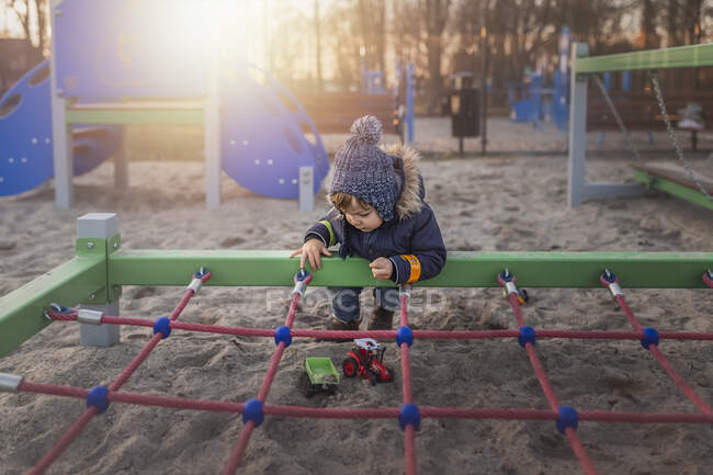 Criança do sexo masculino em um parque infantil em roupas quentes e brincando — Fotografia de Stock