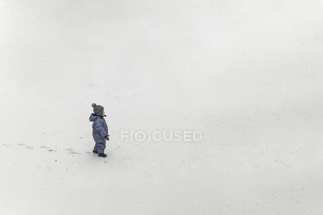 Small boy in blue winter clothes onesie standing on a snow and l — Stock Photo