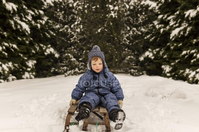 Хлопчик-малюк сидить на санях ковзання зі снігового поля в — стокове фото