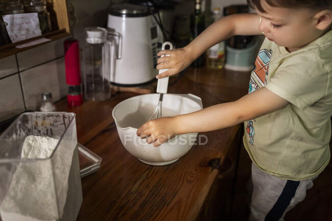 Bambino ragazzo montando e mescolando torta di burro in ciotola bianca con w — Foto stock