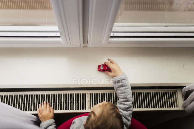 Menino pequeno brincando com carro de brinquedo vermelho no peitoril da janela branca — Fotografia de Stock