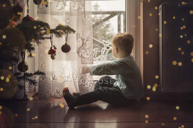 Menino de criança sentado no chão junto à janela ao lado de um cristo — Fotografia de Stock