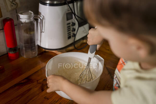 Bambino ragazzo frustate e mescolando torta di burro in ciotola bianca — Foto stock