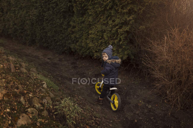 Маленький мальчик в теплой куртке на толкающем велосипеде с желтыми колесами — стоковое фото