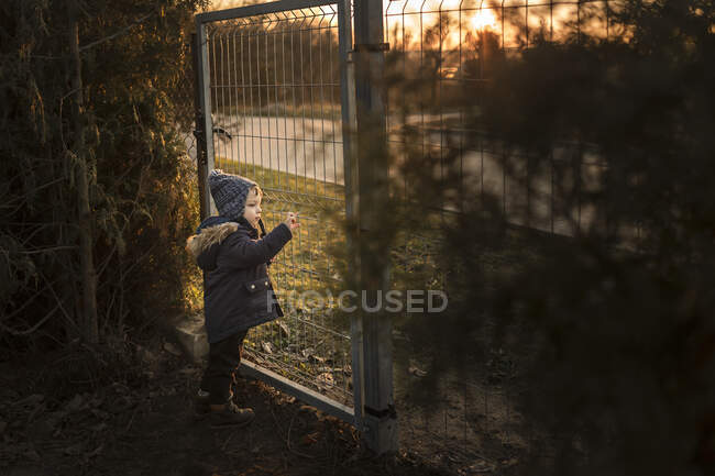Menino pequeno que olha através do portão do jardim fora na estrada — Fotografia de Stock