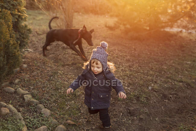 Kleinkind in warmer Jacke und Wollmütze läuft mit Dobermann — Stockfoto