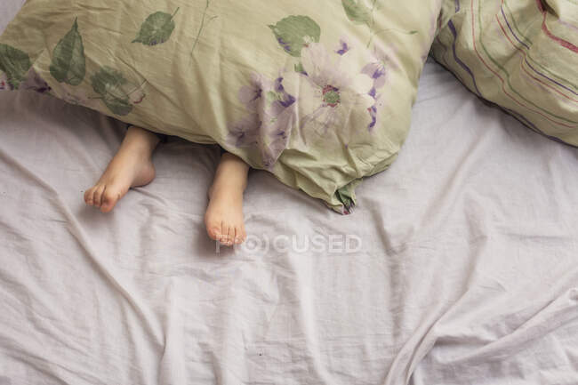 Füße eines kleinen Kindes ragen unter einer Decke hervor — Stockfoto