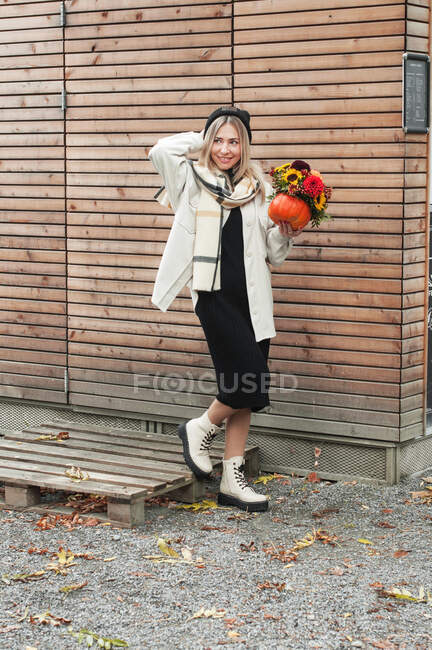 A girl with a bouquet in a pumpkin on the background of a wooden wall. — Stock Photo