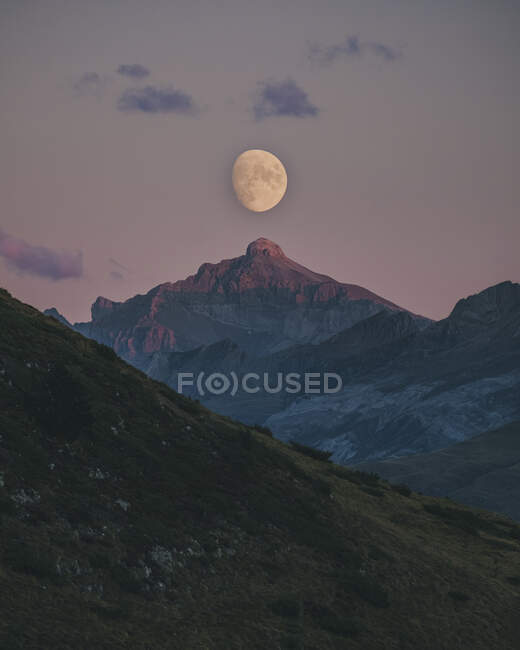 Луна восходит во время заката, выровнявшись с вершиной горы, Пиренеи. — стоковое фото