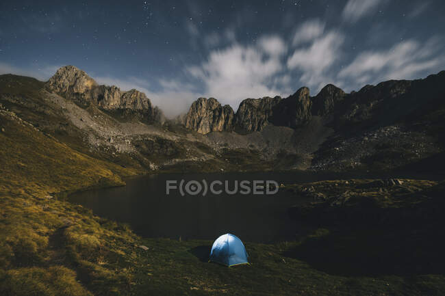 Lighted tent against rugged mountains and lake, Pyrenees. — Stock Photo