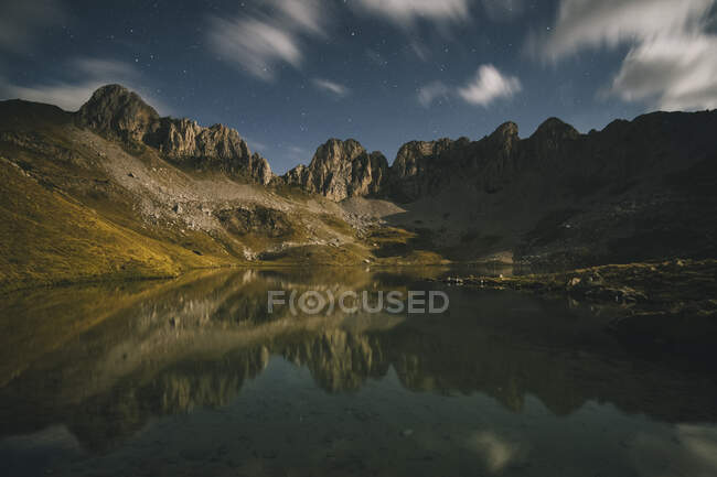 Riflessione di montagna in un lago di notte contro nuvole e stelle, Pirenei. — Foto stock