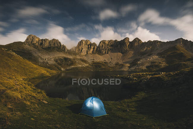 Tenda illuminata contro aspre montagne e lago, Pirenei. — Foto stock