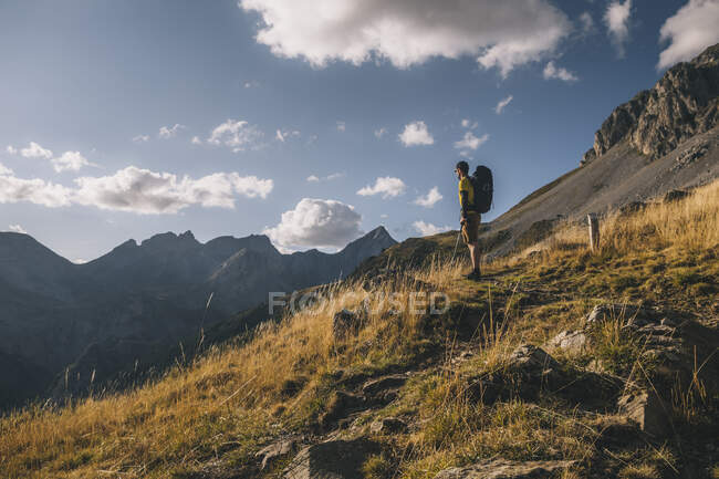 El hombre se detiene en el sendero para admirar la belleza de las montañas de los Pirineos contra el cielo nublado, Aragón España - foto de stock