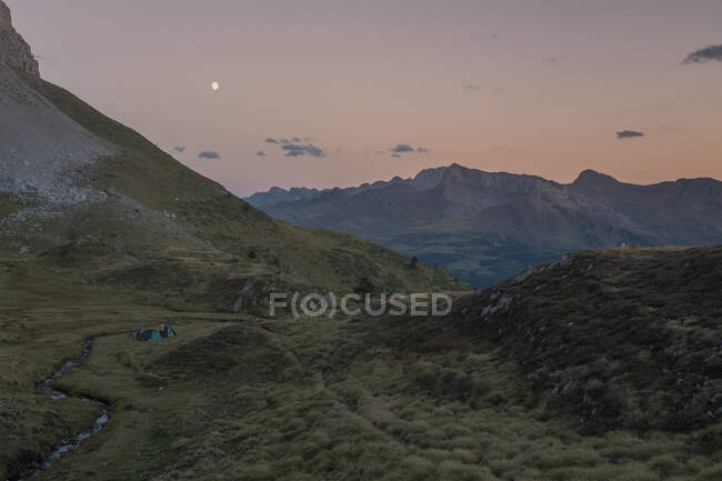 Un groupe de jeunes avec des tentes regardant le coucher du soleil tandis que la lune se lève, Les Pyrénées, Aragon, Huesca — Photo de stock