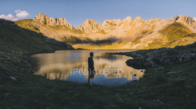 Hombre de pie junto al lago contra los picos escarpados en las montañas del Pirineo al atardecer, Aragón, España - foto de stock