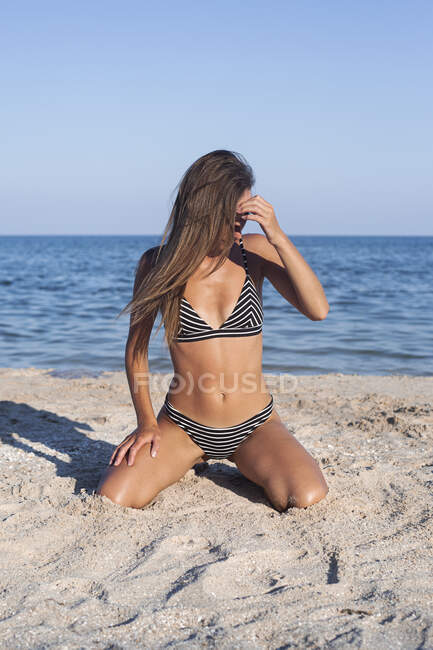 Junge Frau im Badeanzug sitzt am Sandstrand. — Stockfoto