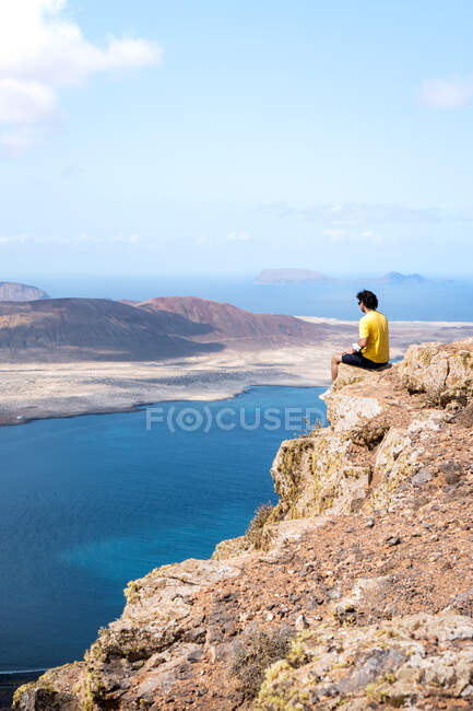 Uomo adagiato su una scogliera con vista sull'isola di La Graciosa, Isole Canarie — Foto stock