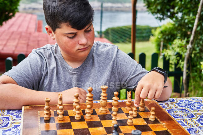 Молодой задумчивый мальчик сидит за шахматной доской и двигает одну из фигур. — стоковое фото