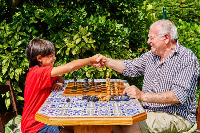 Avô e neto apertando as mãos sobre o tabuleiro de xadrez — Fotografia de Stock