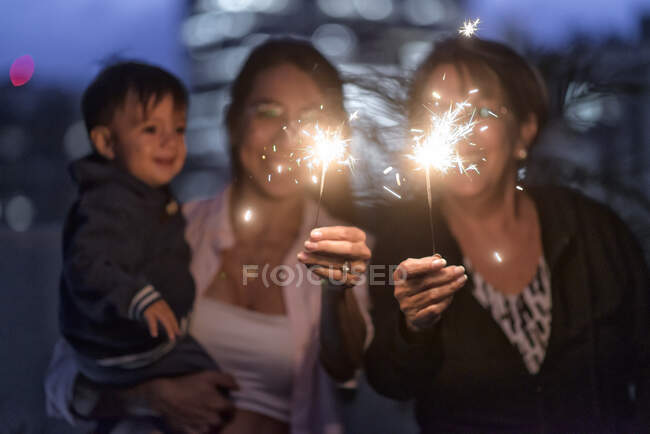 Latino Mother Grandmother and baby boy celebrating christmas new year holidays having fun with sparklers at dawn. — Stock Photo