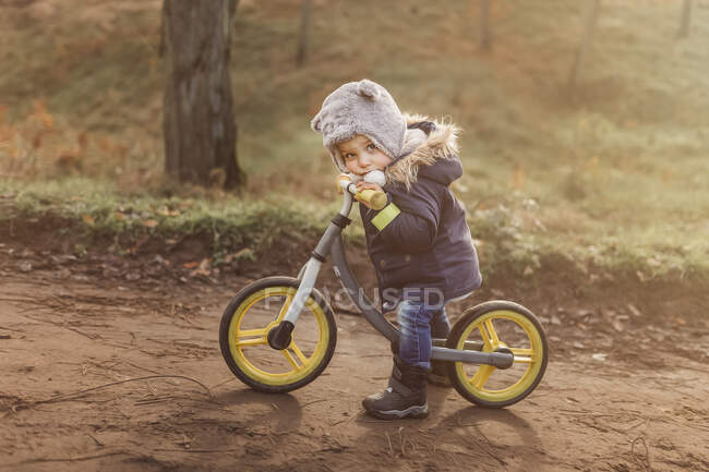 Pequeno menino cansado na floresta sentado em sua bicicleta push com w amarelo — Fotografia de Stock