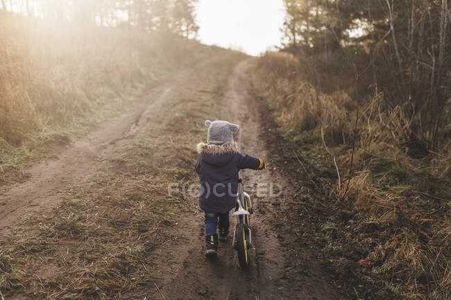 Chico empujando su bicicleta cuesta arriba en el bosque - foto de stock