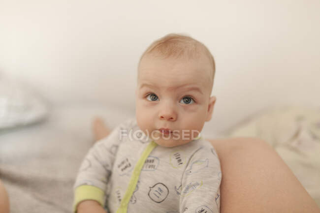 Bambino bambino bambino in tutina seduto sul letto sostenuto — Foto stock