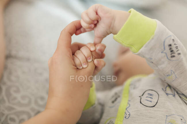 Немовля тримає матір'ю руку і палець, лежачи на ліжку — стокове фото