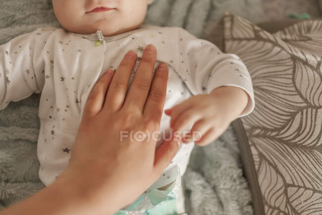 Mão da mãe no peito do bebê pequeno que está deitado na cama — Fotografia de Stock