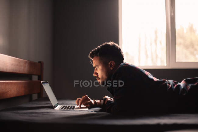 Seriöser Mann benutzt Laptop, der zu Hause im Bett liegt — Stockfoto