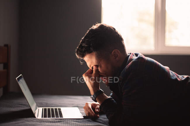 Cansado homem usando computador portátil deitado na cama em casa — Fotografia de Stock