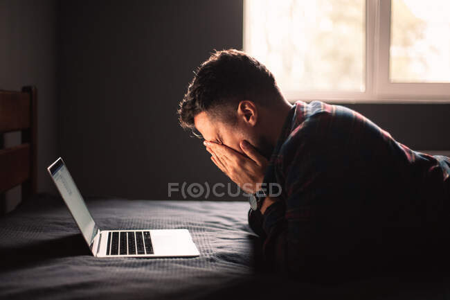 Tired man using laptop computer lying on bed at home — Stock Photo