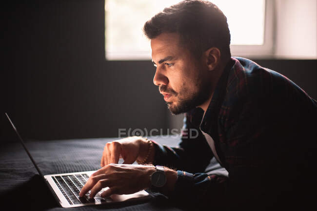 Konzentrierter Mann benutzt Laptop, der zu Hause im Bett liegt — Stockfoto