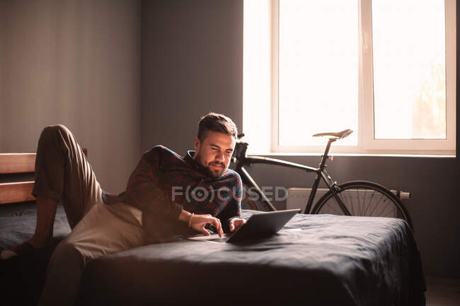 Homem feliz usando computador portátil na cama em casa — Fotografia de Stock