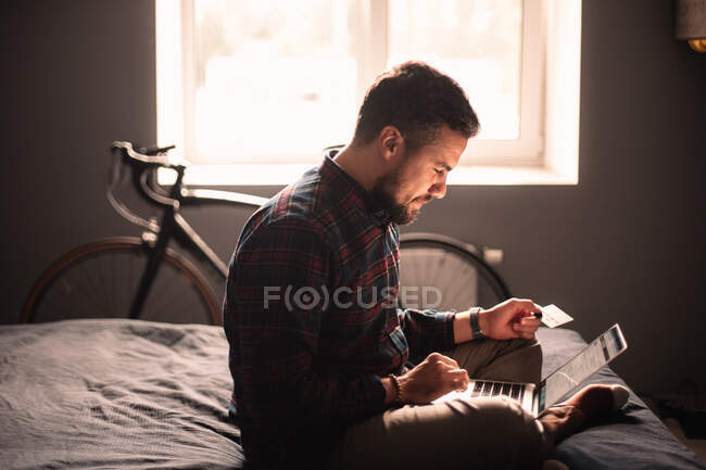 Happy man using credit card and laptop computer shopping online at home — Stock Photo