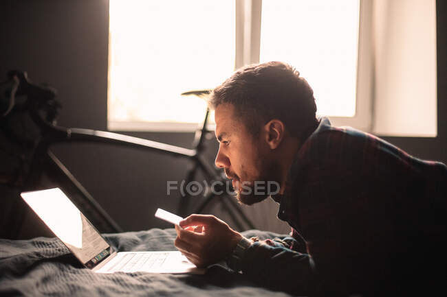 Man using credit card and laptop computer shopping online at home — Stock Photo