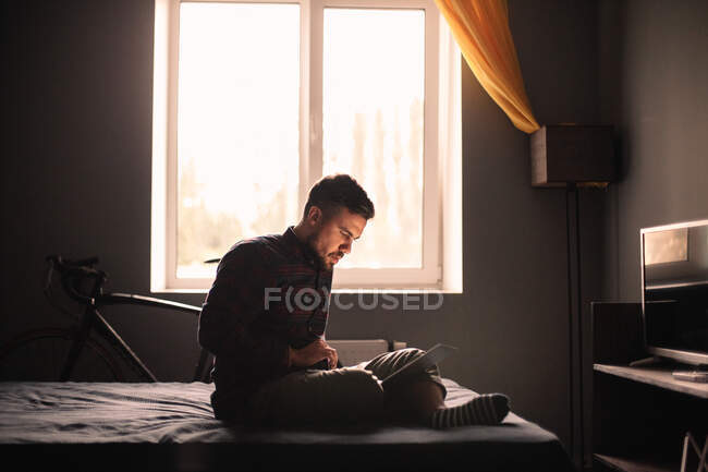 Человек с ноутбуком сидит на кровати дома — стоковое фото