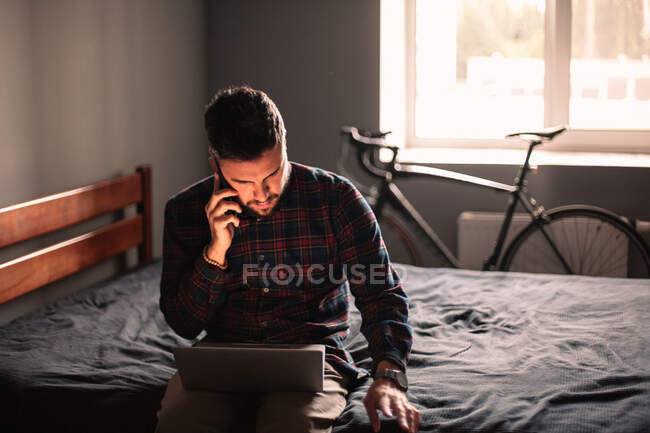 Uomo d'affari che parla su smartphone mentre utilizza il computer portatile a casa — Foto stock