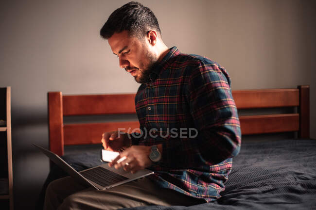 Uomo che utilizza computer portatile e smartphone a casa — Foto stock