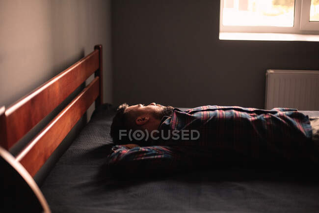 Thoughtful man looking through window lying on bed at home — Stock Photo