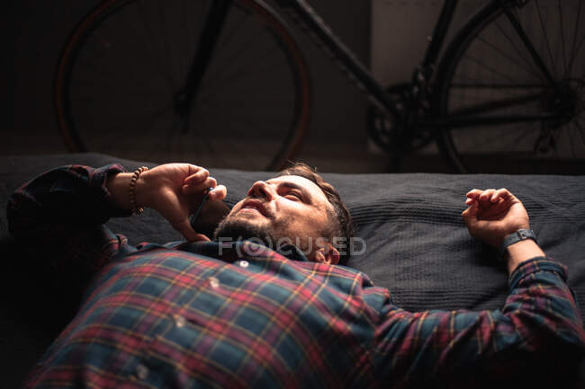 Homem feliz falando no telefone inteligente deitado na cama em casa — Fotografia de Stock