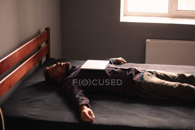 Homem dormindo com laptop em seu peito deitado na cama em casa — Fotografia de Stock