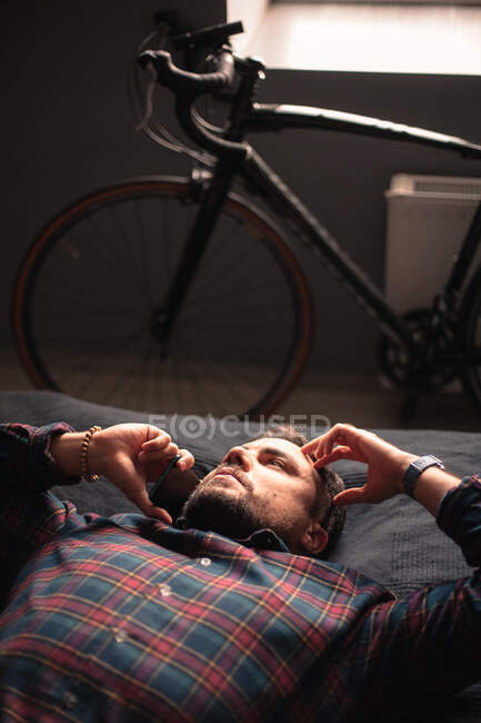 Homem atencioso falando no telefone inteligente deitado na cama em casa — Fotografia de Stock