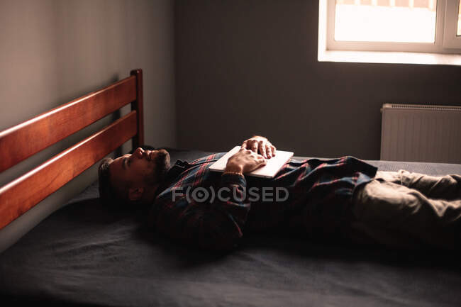 Уставший мужчина с ноутбуком лежит на кровати дома — стоковое фото