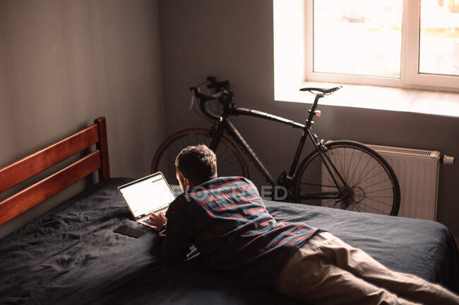 Mann benutzt Laptop, der zu Hause auf Bett liegt — Stockfoto