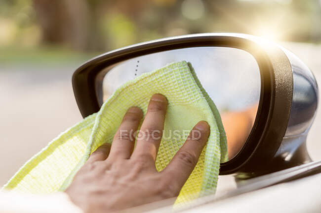 Espejo retrovisor del coche de la limpieza de la mano del hombre usando tela de microfibra. Detalle del concepto del coche de la limpieza - foto de stock