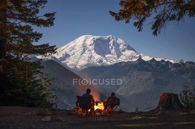 Casal acampando sentado no acampamento em um dia quente de inverno com tenda e uma fogueira no fundo — Fotografia de Stock