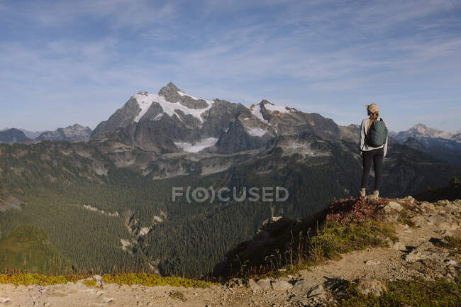 Un hombre con una chaqueta blanca y una mochila está de excursión en las montañas - foto de stock