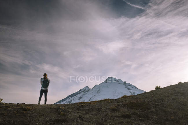 Un hombre con una chaqueta blanca y una mochila de pie en un camino de montaña - foto de stock