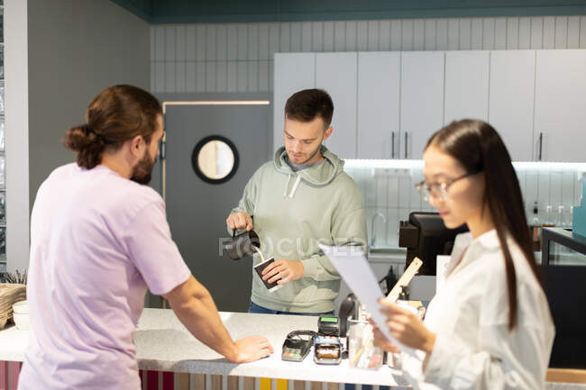 Male barista pouring milk into cup while preparing coffee for customers in queue — Stock Photo